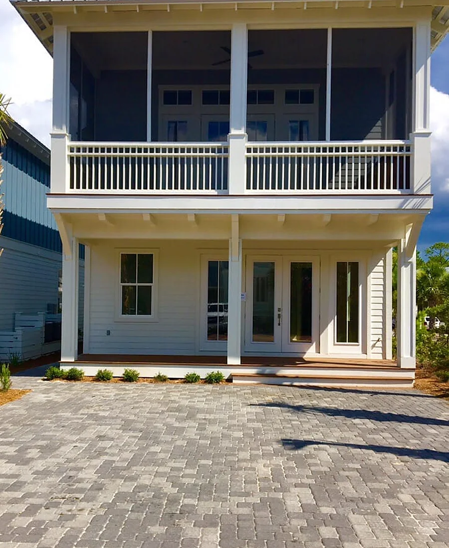 A paver patio laid at the back of a house, running up to a screened porch with a white balcony above it