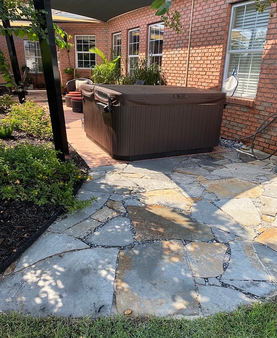 An irregular flagstone patio in gray and cream laid through a planted bed, with a hot tub at the far end