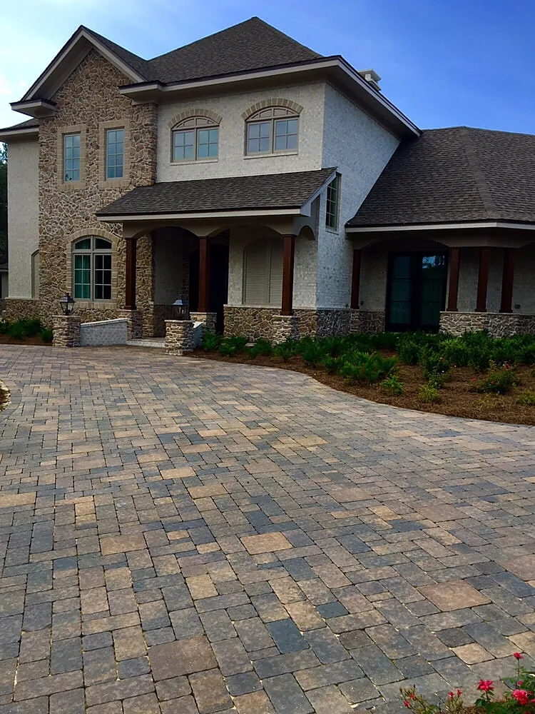 A paver driveway curving up to a stone-and-stucco house, shot down the length of the drive