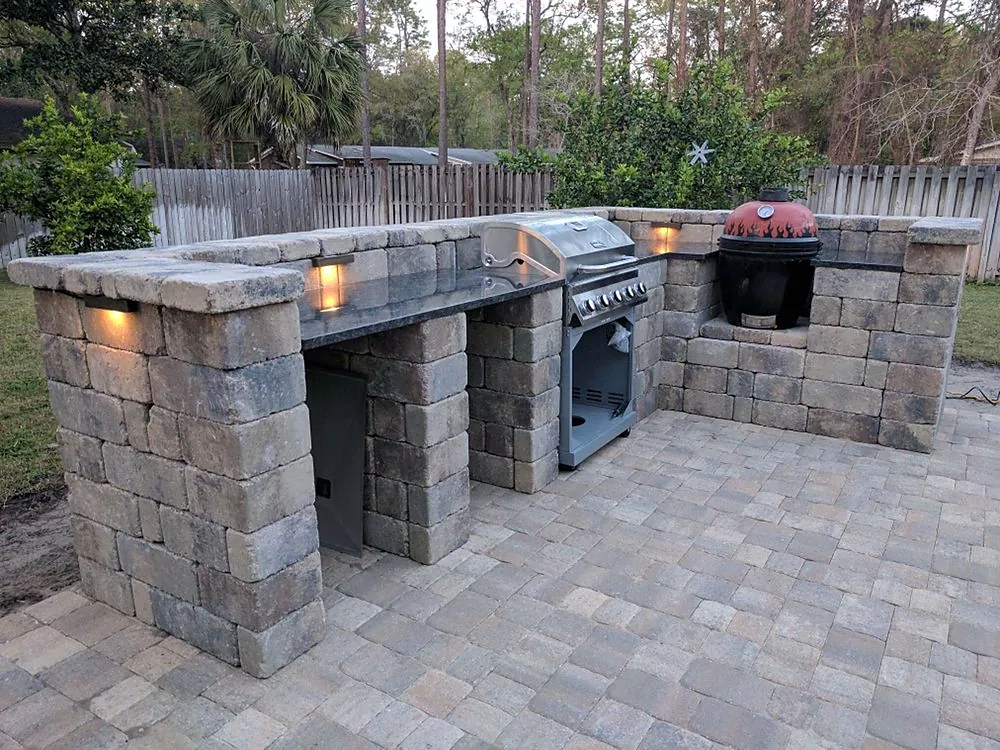 The same outdoor kitchen at dusk, the counter and appliance faces lit from above