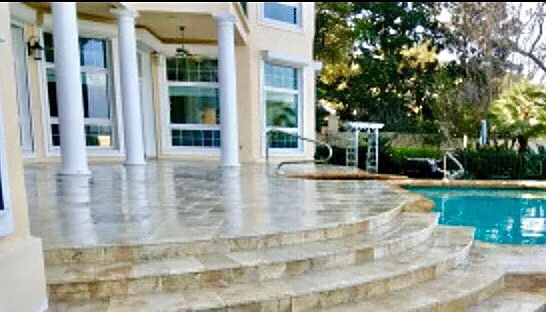 Wide travertine steps in cream running down in shallow rises beside white columns toward a pool