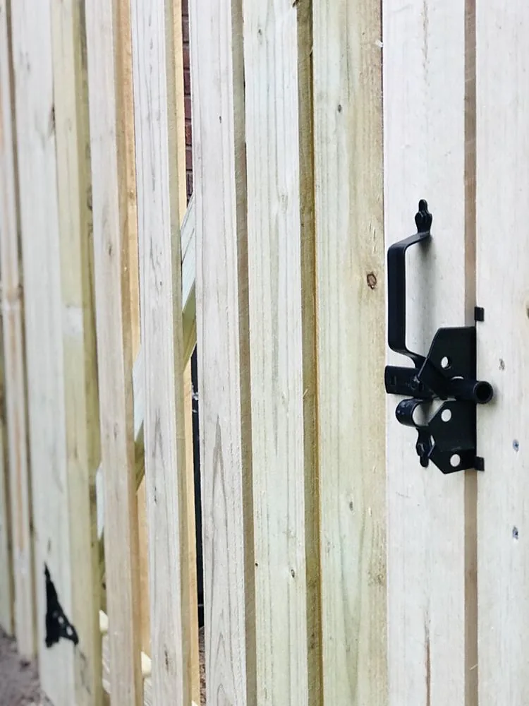 A close view of a timber gate showing the black strap hinge and the latch hardware set into the boards