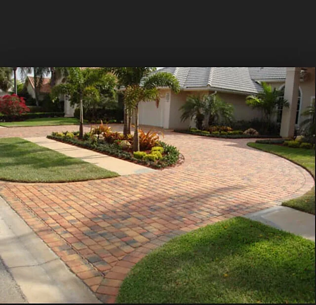 A curving paver run in red, tan and cream, swinging between a lawn and a bed of palms